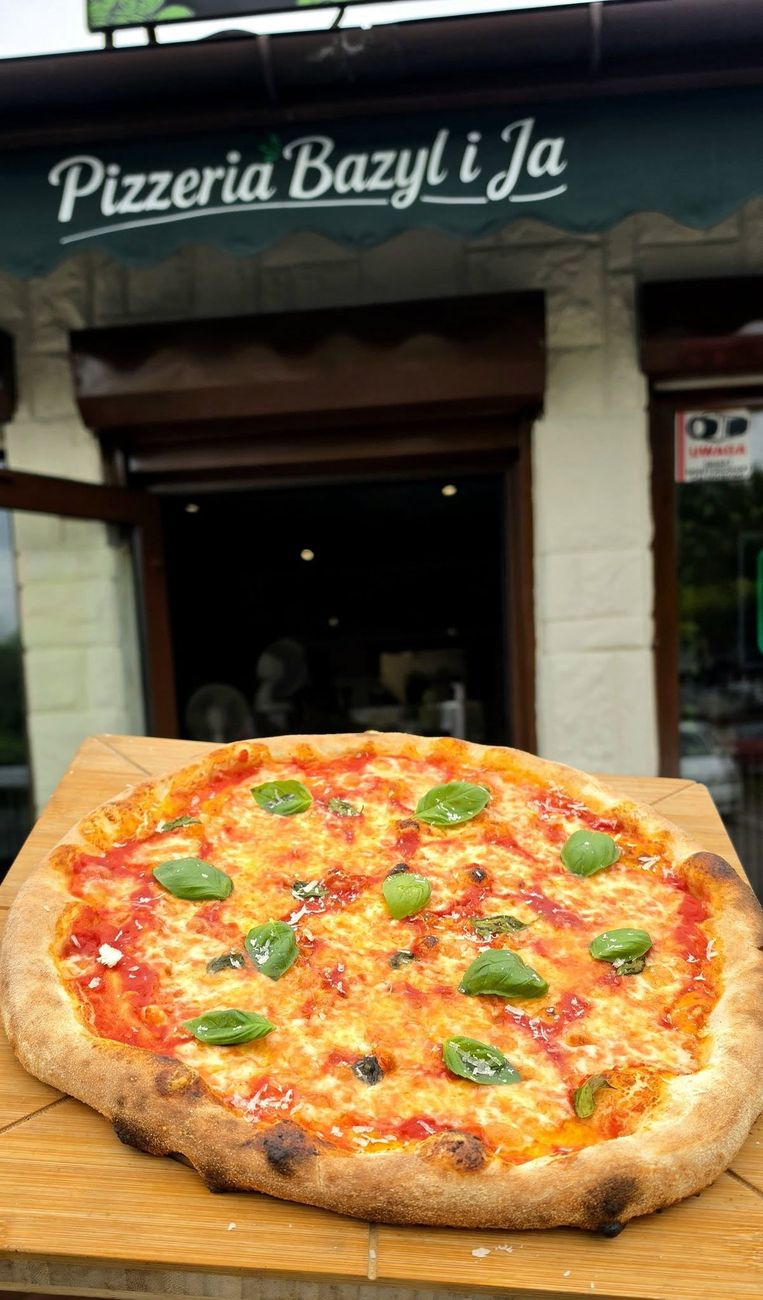 Wejście do Pizzerii Bazyl i Ja z zielonym szyldem, z przodu pizza Margherita